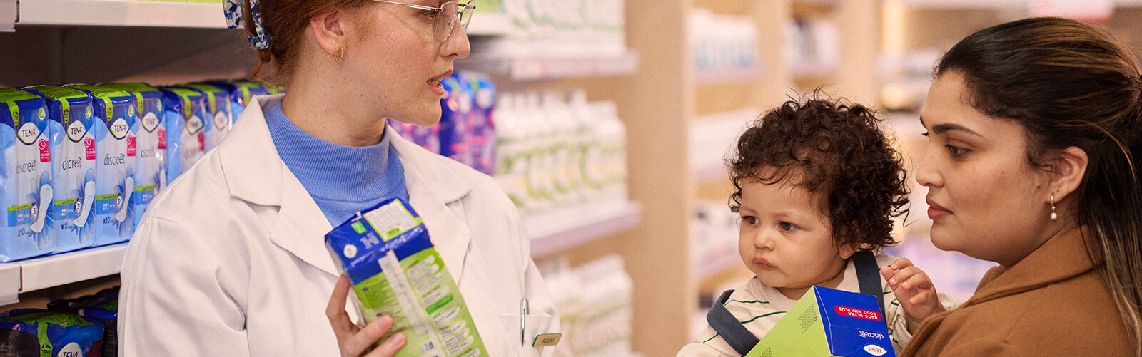 Femme et pharmacien près d’un rayon discutant de TENA Femme et pharmacien près d’un rayon discutant de TENA